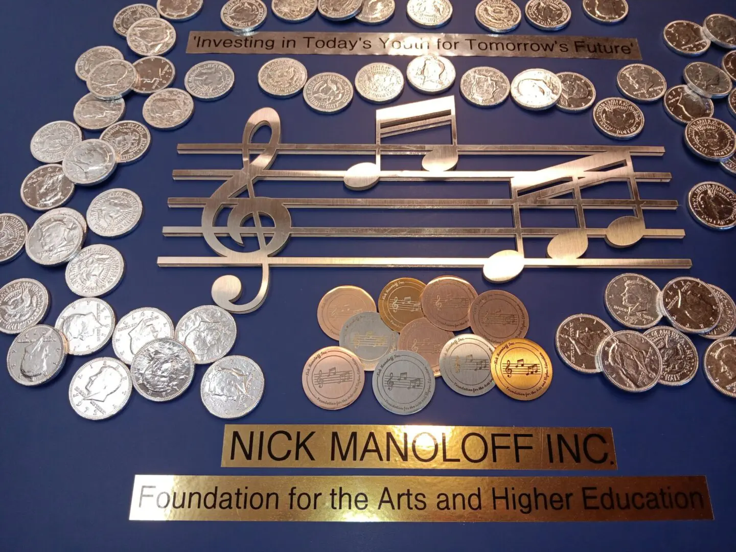 A golden music-themed plaque with a treble clef, musical notes, and coins, honoring Nick Manoloff Inc Foundation for the Arts and Higher Education.
