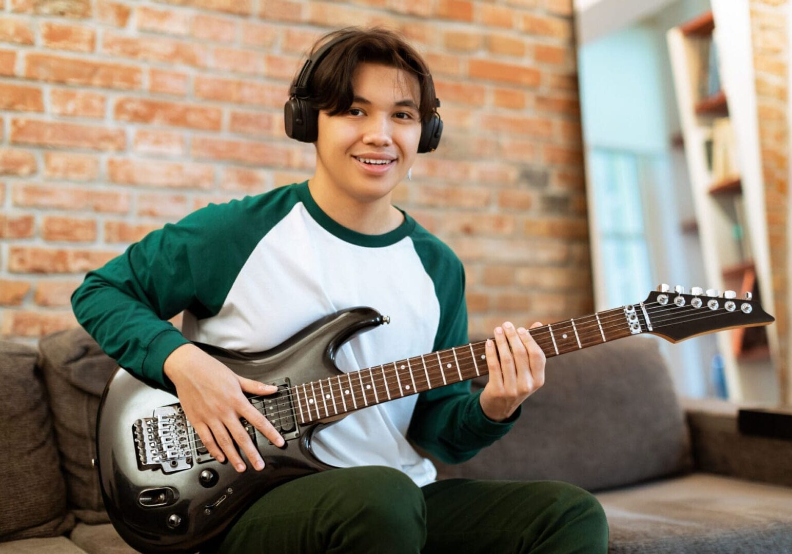 Young man smiling while playing electric guitar indoors.